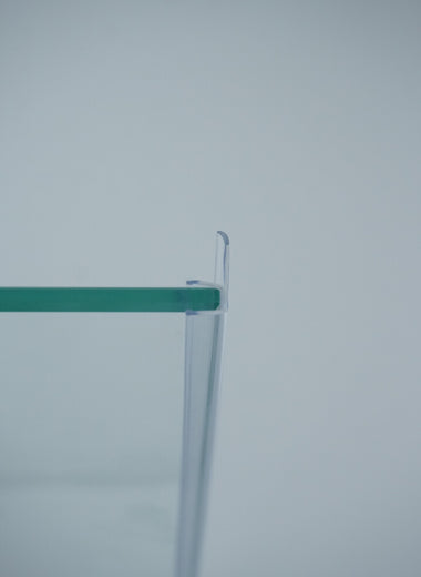 Nahaufnahme einer Dichtleiste der Marke HÜPPE, transparentes, schmales, längliches, U-förmiges, Kunststoffprofil, mit einem Ablaufschutz an der Profilvorderseite, montiert an Glasdusche, vor hellem Hintergrund, Seitenansicht links.
