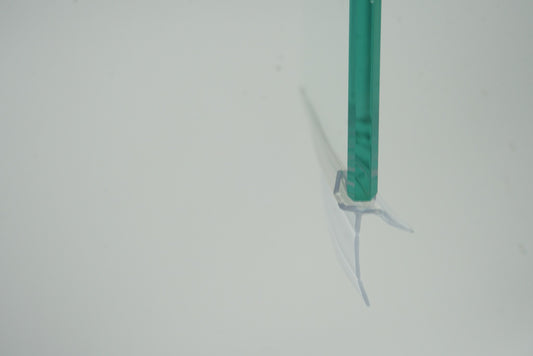 Nahaufnahme einer Ablaufleiste der Marke HÜPPE, transparentes, schmales, längliches, U-förmiges Kunststoffprofil, mit einem Ablaufschutz an der Profilunterseite, montiert an der Unterseite einer Glasdusche, vor weißem Hintergrund, Seitenansicht.
