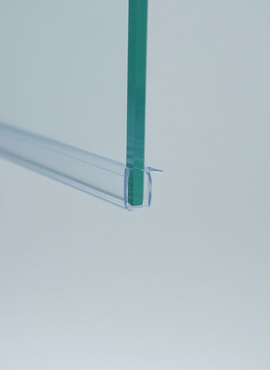 Nahaufnahme einer Ablaufleiste der Marke HÜPPE, transparentes, schmales, längliches, U-förmiges Kunststoffprofil, mit einem Vorsprung an der rechten Profiloberkante, montiert an der Unterseite einer Duschkabine, vor weißem Hintergrund, Seitenansicht links.
