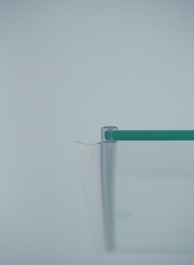 Nahaufnahme einer Dichtleiste der Marke HÜPPE, transparentes, schmales, längliches, U-förmiges Kunststoffprofil, mit einem Ablaufschutz an der Profilvorderseite, montiert an der linken Außenkante einer Glasdusche, vor weißem Hintergrund.
