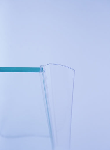 Nahaufnahme einer Anlagenleiste der Marke HÜPPE, transparentes, schmales, längliches, U-förmiges, Kunststoffprofil, mit einem Ablaufschutz an der Profilvorderseite, montiert an Glasdusche, vor weißem Hintergrund, Seitenansicht links.
