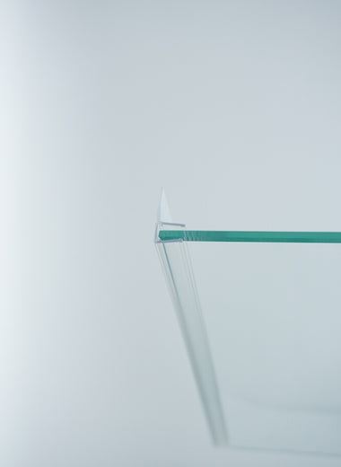 Nahaufnahme einer Dichtleiste der Marke HÜPPE, transparentes, schmales, längliches, U-förmiges Kunststoffprofil, mit einem Ablaufschutz an der Profilvorderseite, montiert an der linken Außenkante einer Glasdusche, vor weißem Hintergrund.
