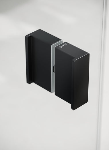 Nahaufnahme einer Duschkabine mit einem schwarzen, matten, rechteckigen, minimalistischen, HÜPPE Komfortgriff im Fokus, vor einem hellen Hintergrund.