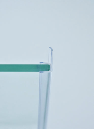 Nahaufnahme einer Dichtleiste der Marke HÜPPE, transparentes, schmales, längliches, U-förmiges, Kunststoffprofil, mit einem Ablaufschutz an der Profilvorderseite, montiert an Glasdusche, vor hellem Hintergrund, Seitenansicht links.